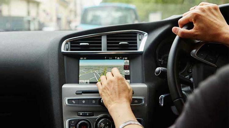 Person in a vehicle, one hand on the steering wheel and one interacting with an onboard telematics device.